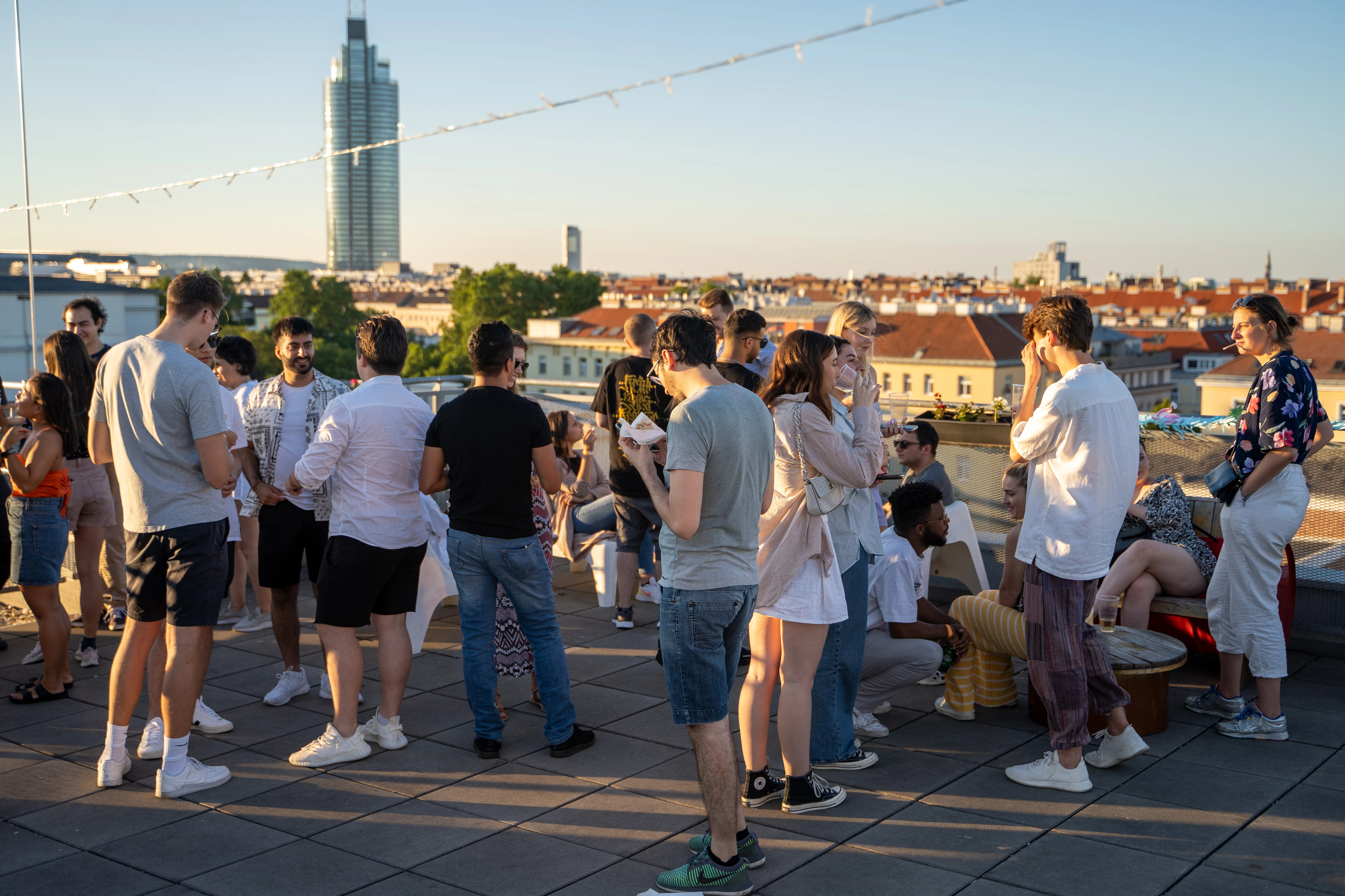 © Junger Leute Dachparty im Sonnenuntergang, Stadt im Hintergrund.